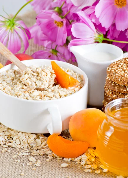 Haferflocken mit Aprikose, Milchkanne, Keksen, Honig und Blumen — Stockfoto