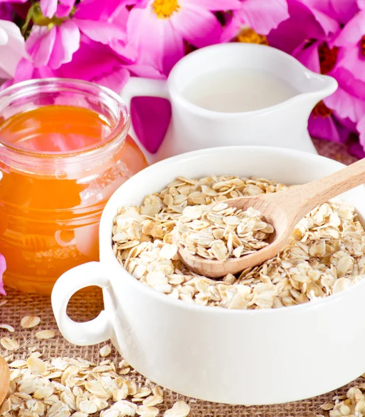 Oatmeal, honey, milk jug and flowers — Stock Photo, Image