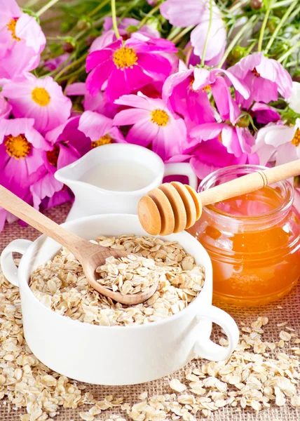 Farinha de aveia, mel, jarro de leite e flores — Fotografia de Stock