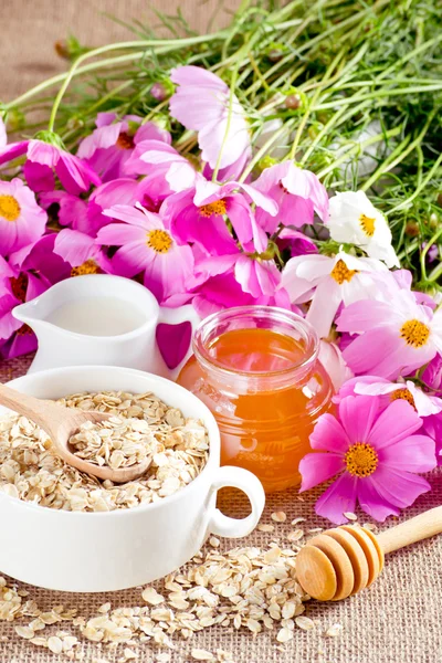 Oatmeal, honey, milk jug and flowers — Stock Photo, Image