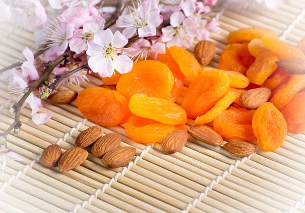 Dried apricots with almonds and blossoming branch on bamboo napk — Stock Photo, Image