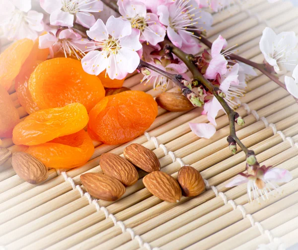 Gedroogde abrikozen met amandelen en bloeiende tak op bamboe napk — Stockfoto