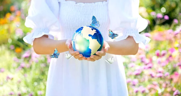 Earth Day or World Environment Day concepts. Save our home Planet, protect Green Nature and ecology, sustainable lifestyle, Climate themes. Woman in white dress holding globe in hands and butterflies.