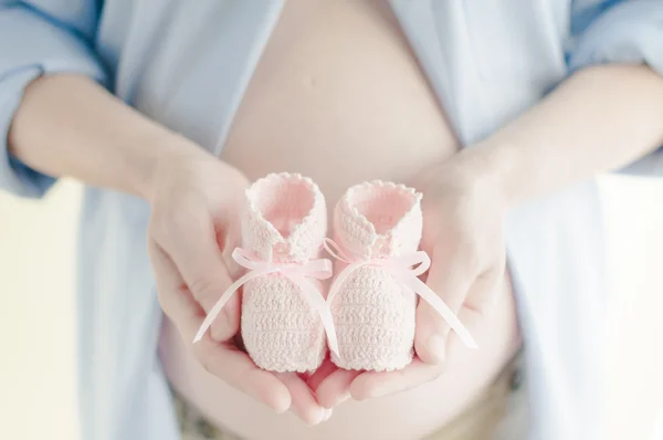 妊娠中の女性は彼女の子供の最初靴を保持しています。 ストック画像