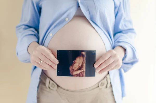 hamile kadının hamile karnı üzerinde ultrasonik fotoğraf tutarak yakın çekim