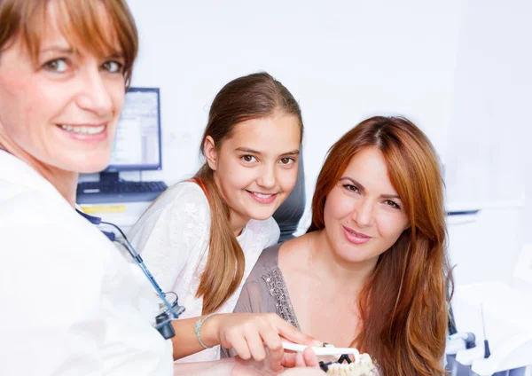 Un medico dei denti delle donne spiega una madre con un bambino come lavarsi i denti — Foto Stock