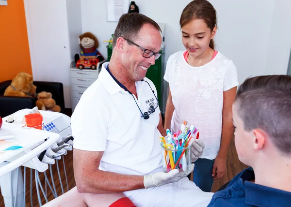 Doctor mostrando a una adolescente y un niño cómo tienen que usar el cepillo — Foto de Stock