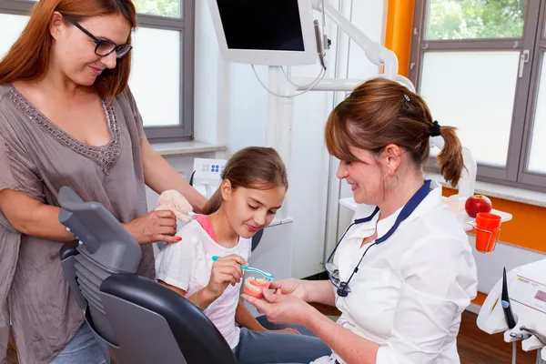 Un médico explica a una familia joven cómo pueden cuidar los dientes — Foto de Stock