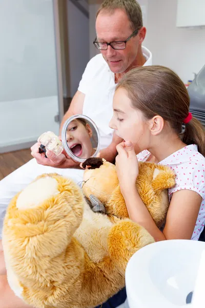 En læge forklarer en ung mor og datter, hvordan de kan pleje tænder - Stock-foto