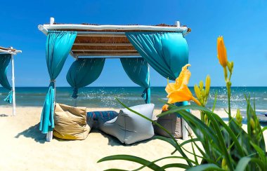   Sarı çiçekler mavi çadır hasır şemsiyeler ve ahşap iskemleler yatak üzerinde ahşap masa mavi gökyüzü tropikal deniz, Yunanistan 'da plaj tatil beldesinde beyaz kum