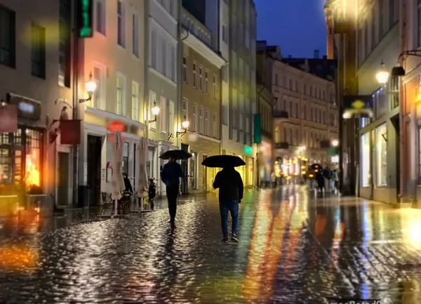 人々シルエットで傘が歩く夜の路上でぼやけた街の光の反射ランタンとタリン旧市街の店のつる — ストック写真