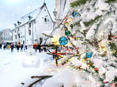 Noel ağacı süslenmiş kırmızı top ve kar yağışlı kış gününde insanlar sokaklarda yürür aydınlanmış kar taneleri ortaçağ şehir evlerinin çatılarında kar altında Estonya 'daki Tallinn Eski Şehir Tatili' nde