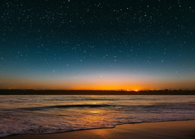 blue bright starry sky on pink yellow sunset at sea water vawe reflection blurred light full moon moonlight  skyline  nebula nature background 