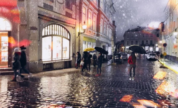 雨の夜の通りの人々は ヨーロッパへのタリン旧市庁舎広場旅行でアスファルトの上に雨の夜の通りの人々は傘ボケぼやけた夜の光ぬれた舗装中世の家の窓の反射と歩く — ストック写真