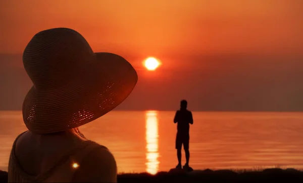 Femmes en paille chapeau sur orange mer coucher de soleil sur horizon homme silhouette regarder soleil aube nature paysage romantique été fond — Photo