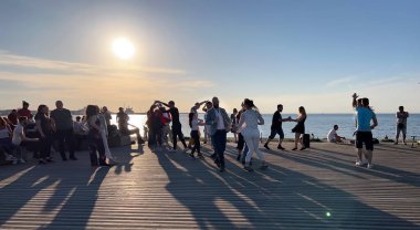 İnsanlar gün batımında Baltık sahilindeki gezinti alanında dinleniyor ve dans ediyor.