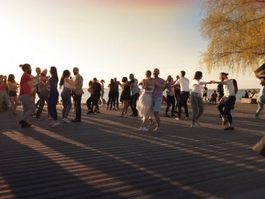İnsanlar gün batımında Baltık sahilindeki gezinti alanında dinleniyor ve dans ediyor.
