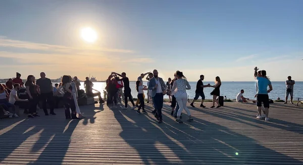 İnsanlar gün batımında Baltık sahilindeki gezinti alanında dinleniyor ve dans ediyor.