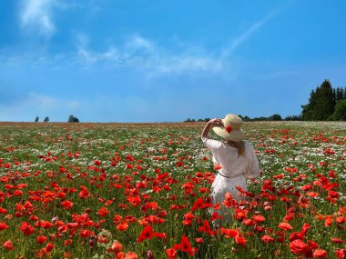 Kırmızı gelincik ve papatya çiçekleriyle vahşi sahada zarif bir kadın gökkuşağı mavi gökyüzü manzarası
