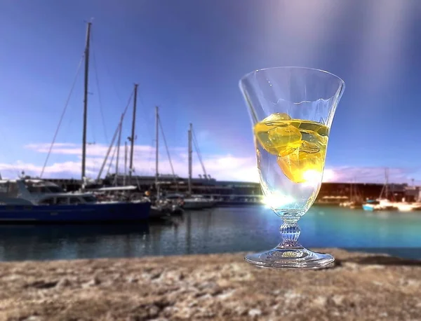 glass of water  with lemon with sun beam  in cafe  on promenade harbor ,boat on sea  blue sky and sea water summer nature landscape