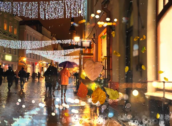 rain city  Autumn leaves  cold weather rainy drops on window and people silhouette with umbrellas night  traffic  light blurred reflection cold season view from window glass vitrines Tallinn Old Town