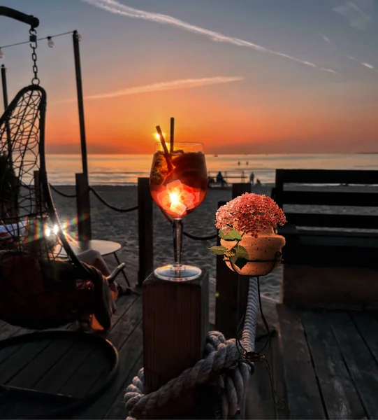 orange sunset  resort at sea flowers in decorative cup and glass of juice on wooden table top in beach restaurant view in pink sky and sea nature landscape