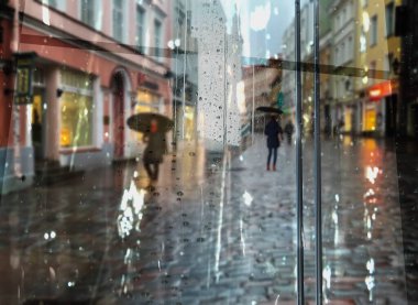 rain in  city street, people silhouette with umbrellas ,modern and vintage building ,Rainy weather season ,Autumn leaves on window,wet drops ,night  blurred light  reflection cold urban  defocus   background 