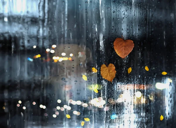 rain in  city street, people silhouette with umbrellas ,modern and vintage building ,Rainy weather season ,Autumn leaves on window,wet drops ,night  blurred light  reflection cold urban  defocus   background