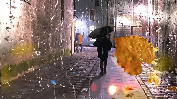 Autumn rainy city ,Tallinn old town,yellow leaves and  rain drops on wet  window glass ,Rainy weather, pedestrian with umbrella ,  bokeh bluured night city light  ,cold  season background template banner