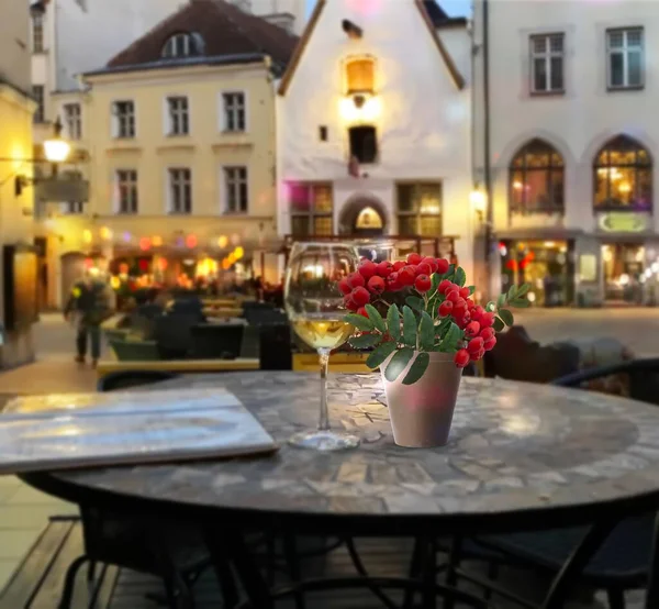 Evening street cafe glass of wine and red  rowan ash berry branch on table ,  people walk evenight blurred light vestive decoration in medieval city Tallinn old town