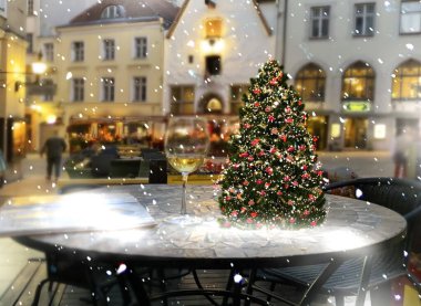    Christmas tree on cafe table  top and glass of wine on snowy festive street in medieval city Tallinn old town