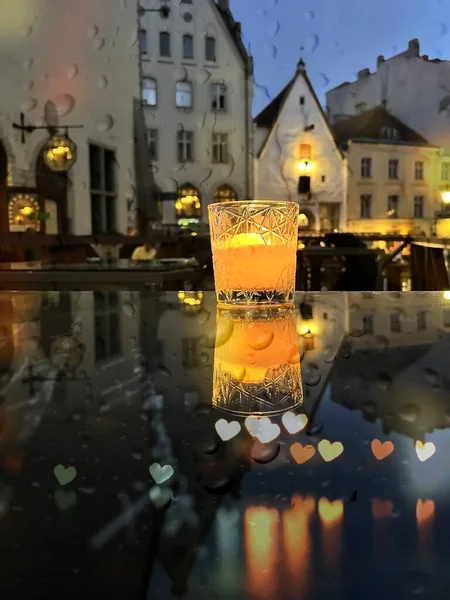 glass cup with candle light on table on medieval street evening cafe  blurred bokeh light under rain drops on window in Tallinn old town Autumn holiday in Estonia