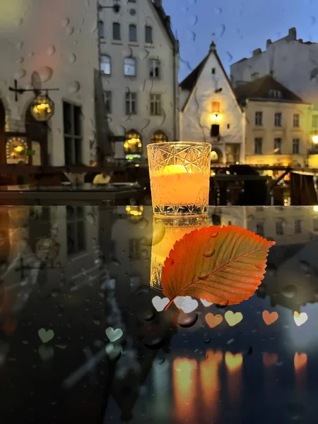 glass cup with candle light on table on medieval street evening cafe  blurred bokeh light under rain drops on window in Tallinn old town Autumn holiday in Estonia