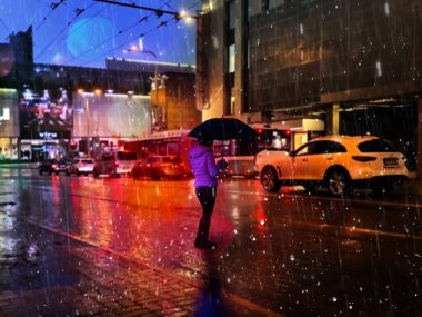 Yağmurlu şehir araba trafiği bulanıklaştı. Şemsiyeli genç kadın gecenin ortasında sonbahar yağmuru