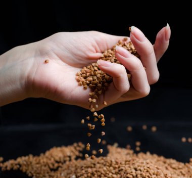 Bir elden çıkan karabuğday, yere düşen karabuğday lapası, arka planda bir dişinin elinde çiğ.