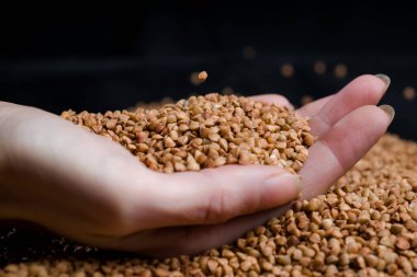 Bir elden çıkan karabuğday, yere düşen karabuğday lapası, arka planda bir dişinin elinde çiğ.