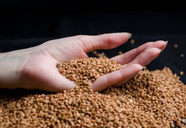 Bir elden çıkan karabuğday, yere düşen karabuğday lapası, arka planda bir dişinin elinde çiğ.