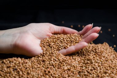 Bir elden çıkan karabuğday, yere düşen karabuğday lapası, arka planda bir dişinin elinde çiğ.