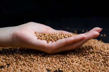 Bir elden çıkan karabuğday, yere düşen karabuğday lapası, arka planda bir dişinin elinde çiğ.