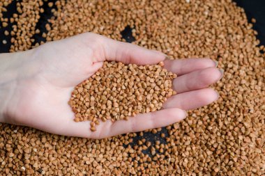 Bir elden çıkan karabuğday, yere düşen karabuğday lapası, arka planda bir dişinin elinde çiğ.