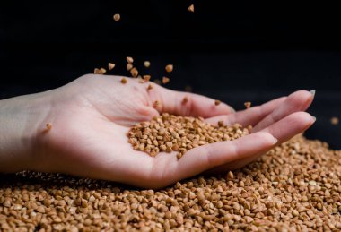 Bir elden çıkan karabuğday, yere düşen karabuğday lapası, arka planda bir dişinin elinde çiğ.