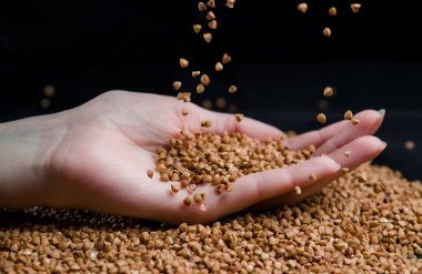 Bir elden çıkan karabuğday, yere düşen karabuğday lapası, arka planda bir dişinin elinde çiğ.