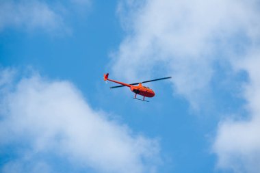 Gökyüzündeki helikopter mavi gökyüzünde kırmızı turuncu helikopter yazın uçuyor.