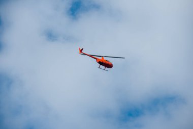 Gökyüzündeki helikopter mavi gökyüzünde kırmızı turuncu helikopter yazın uçuyor.