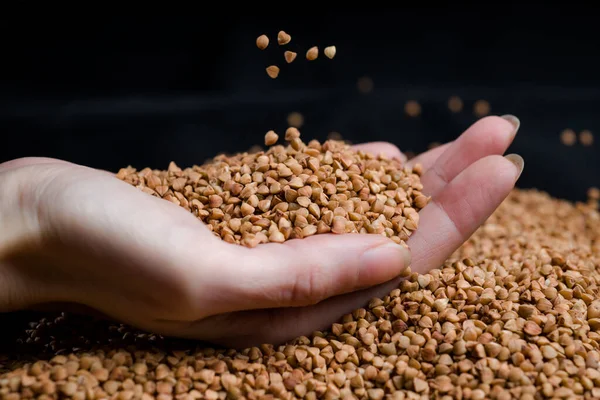 Bir elden çıkan karabuğday, yere düşen karabuğday lapası, arka planda bir dişinin elinde çiğ.