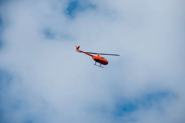 Gökyüzündeki helikopter mavi gökyüzünde kırmızı turuncu helikopter yazın uçuyor.
