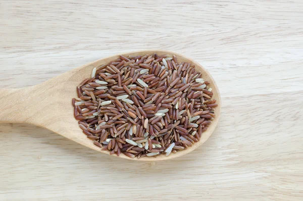 Arroz de jasmim vermelho em uma concha de madeira, na mesa de madeira . — Fotografia de Stock