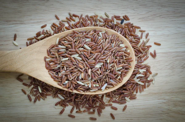 Red jasmine rice in a wooden ladle, on wood table with vignette — Stock Photo, Image