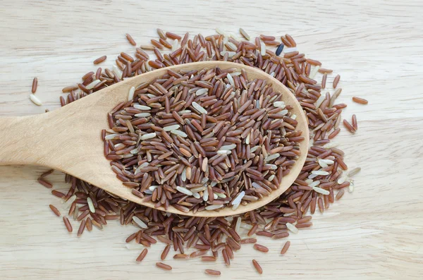 Κόκκινο ρύζι γιασεμί σε μια ξύλινη κουτάλα, σε ξύλινο τραπέζι. — Φωτογραφία Αρχείου