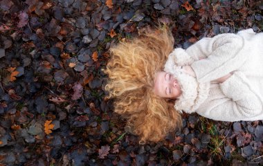 Güzel, seksi, olgun, kızıl saçlı bir kadının portresi. Uzun kırmızı kıvırcık saçlı, çayırda uzanmış, koyu ıslak sonbahar yapraklarıyla kaplı. Kopya alanı.